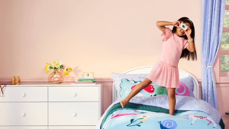 A pink bedroom with colorful unicorn bedding with snails and a butterfly-shaped shelf. Reads: New and only at Walmart. Introducing Mainstays Kids.