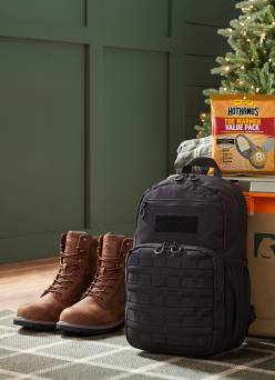 HotHands Toe Warmer Value Pack with a black tactical backpack and brown boots on a rug near a Christmas tree.