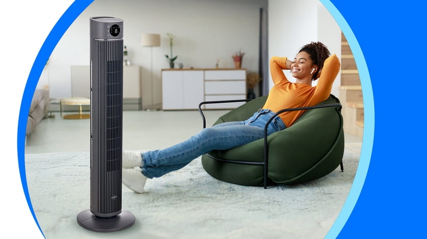 A woman sits on a bean bag chair in front of a Midea tower fan in her apartment.