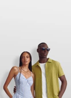 A woman wears a gold necklace and a blue-striped dress and a man wears black sunglasses, a white-shirt and a green button-up.