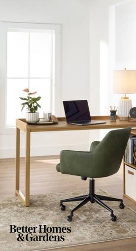 A narrow office desk and chair are placed in front of a window. A lamp, laptop and various office supplies rest on the surface.