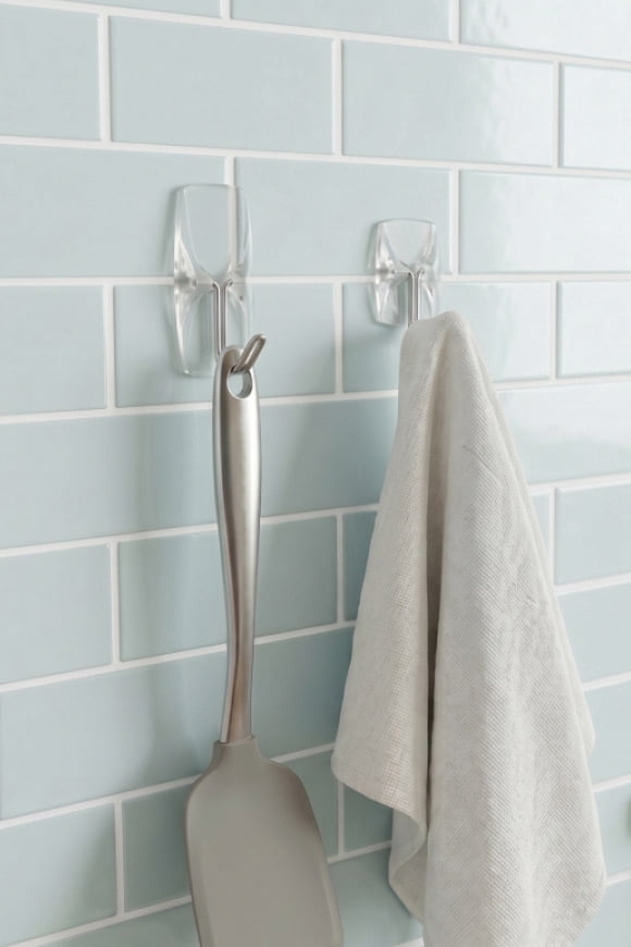 A hand towel and a tool hanging from clear hooks on a blue tiled wall.