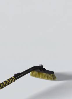 Long handled black and yellow cleaning brush with angled yellow bristles on a plain surface.