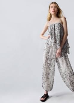 Woman with long blonde hair wearing a black and white printed tiered camisole top and matching balloon leg pants with sandals.
