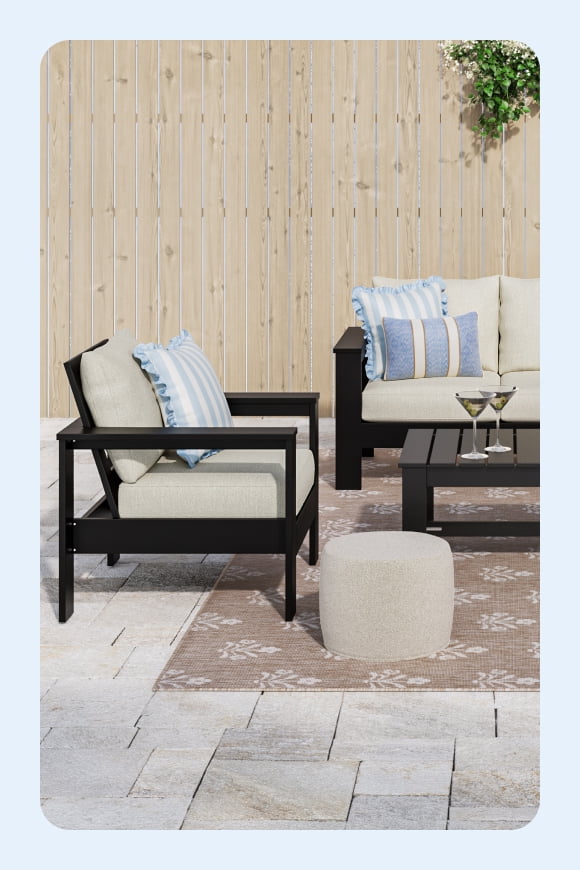 A dark brown metal rectangular patio table with a light blue umbrella. Chairs with white cushions and a blue-and-white striped accent pillow.