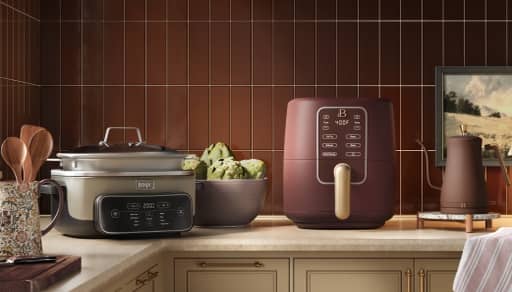 Kitchen counter with slow cooker, air fryer, bowl of artichokes and kettle beside framed wall art.