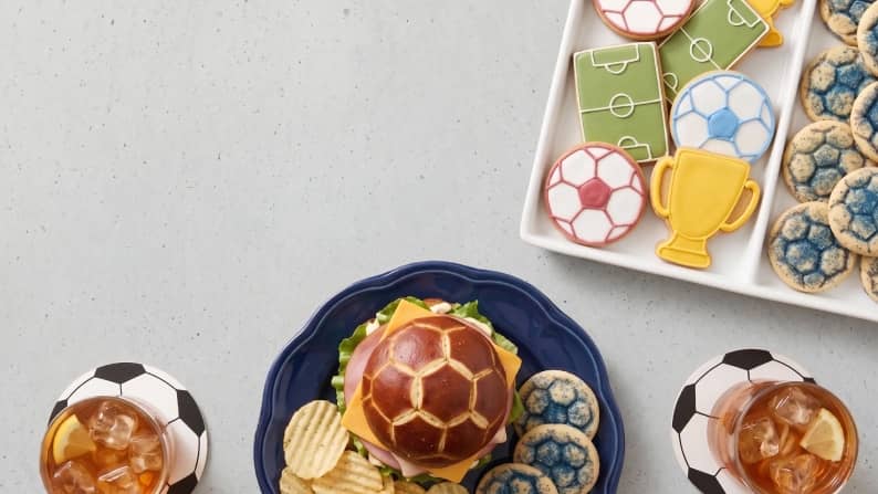 A tray of frosted soccer and trophy cookies next to a burger with a soccer grilled bun top.
