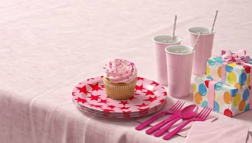 Table setting with pink plates, napkins, cutlery and cupcakes for a celebration.