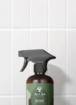 A brown spray bottle with a green label of As I Am formulas for curly hair is on a white tiled background.