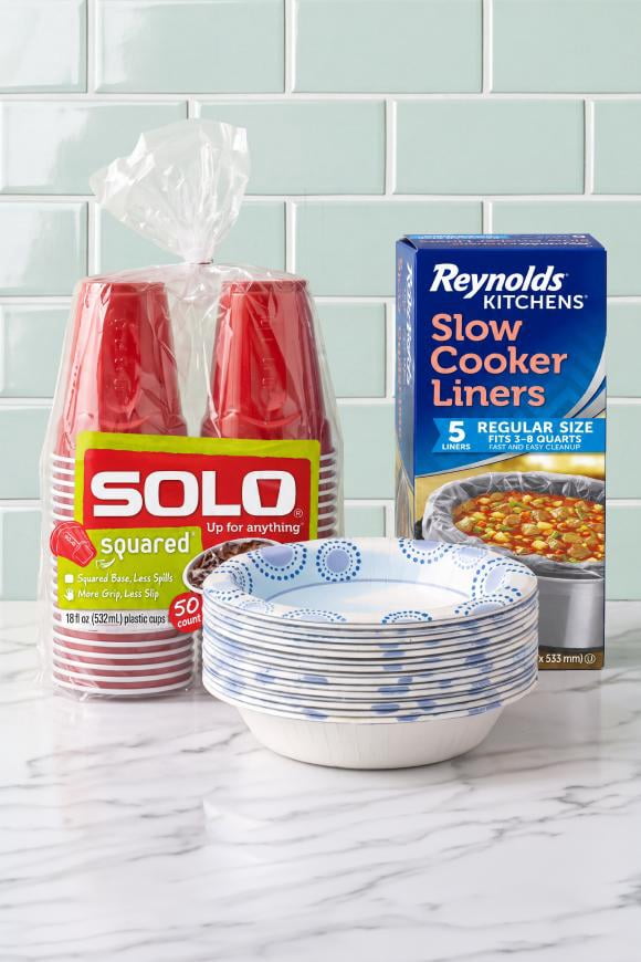 Solo red cups, Reynolds Kitchens Slow Cooker Liners box and a stack of blue and white disposable bowls on a countertop.