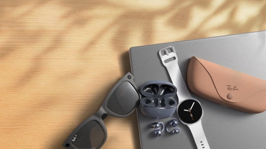 Smart glasses, a smartwatch, earbuds and a sunglasses case resting on a laptop.