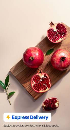 Express Delivery. Subject to availability. Restrictions & fees apply. Whole and cut-up pomegranates on a wooden cutting board on a neutral background.
