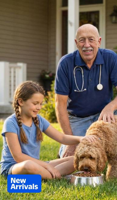 A girl and an older man with a stethoscope (Dr. Pol) petting a brown dog eating from a bowl on a lawn.