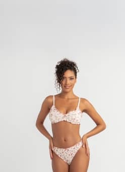 A woman in a white bra and underwear standing in front of a gray background.