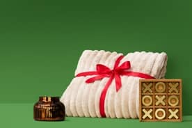 A fuzzy blanket wrapped in a red ribbon is surrounded by a candle and a game of tic tac toe.