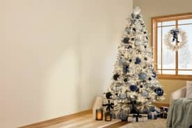 Room shown with a tree decorated in pale blue and dark blue baubles, snowflake ornaments. A white wreath with a blue bow in window also shown.