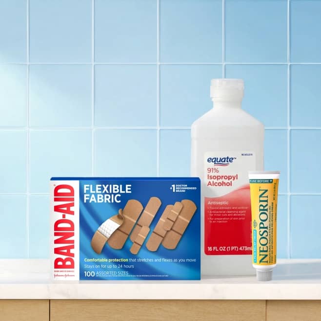 Band Aid flexible fabric bandages box, Equate 91% isopropyl alcohol bottle, and Neosporin antibiotic ointment tube on a counter.