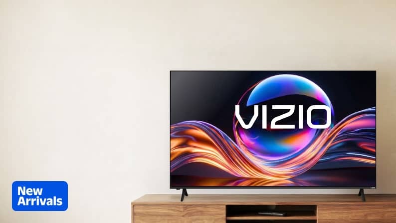New Arrivals logo. VIZIO flatscreen TV on a wooden stand. The TV features the VIZIO logo against a wavy gold, pink and blue design.