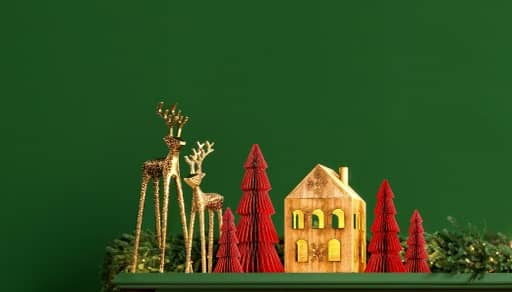 Image of a green painted mantel decorated with gold reindeer, a lit house and green garland.