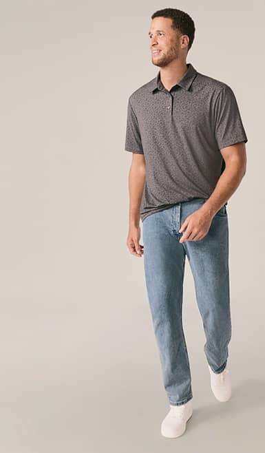 A man wearing jeans and grey polo shirt is pictured on a beige backdrop.
