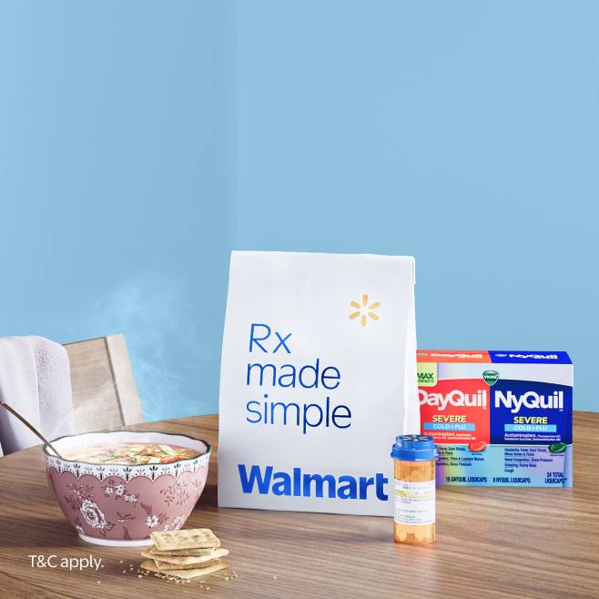 A prescription bag, medication bottle, DayQuil and NyQuil and a bowl of soup with crackers on a table.