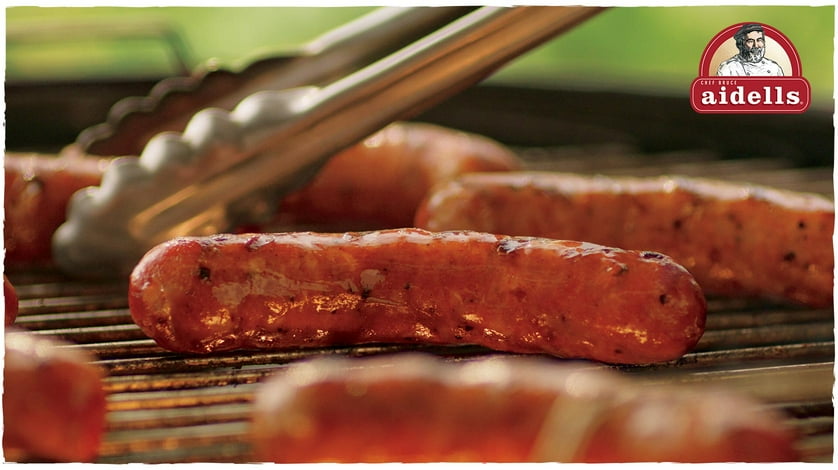 Aidells Chicken and Apple and Cajun Style Andouille smoked sausages roasting on a grill with delicious sear marks.