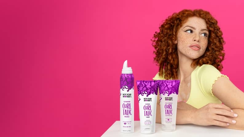 A woman with her arms crossed with three haircare products placed in front of her.