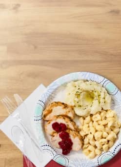 Thanksgiving dinner is shown on a disposable plate with a napkin and utensils on the side.