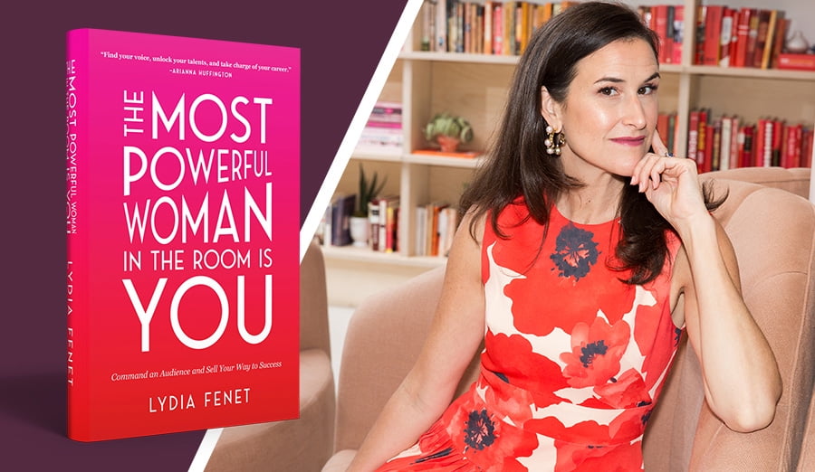 Lydia Fenet in a red and white dress sitting on a couch with a copy of her newest book next to her