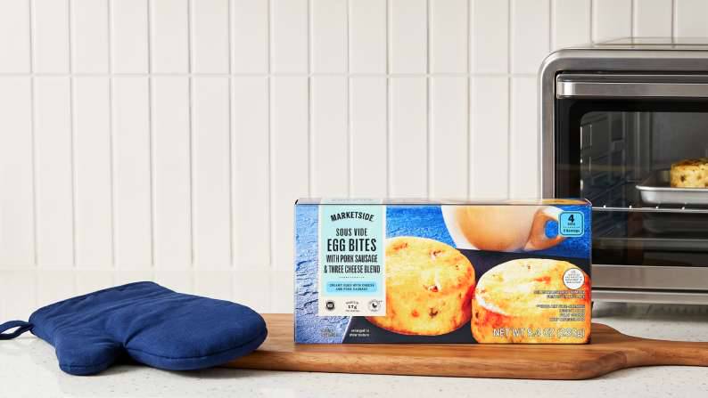 A box of Marketside sous vide egg bites with pork sausage and three-cheese blend on a counter next to an oven mitt and a toaster oven.