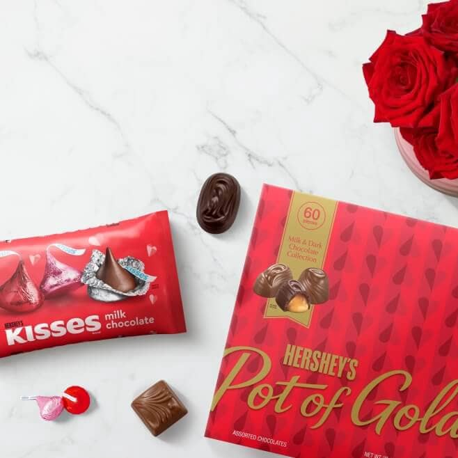 A Hershey’s Pot of Gold chocolate box is shown next to pink & red Hershey’s kisses.