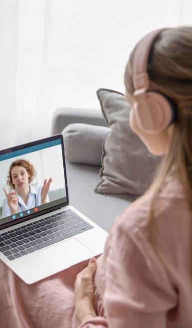 A woman with headphones has a virtual doctor meeting on her laptop.