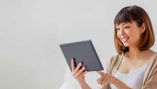 A woman on her couch feels her forehead temperature in front of a tablet.
