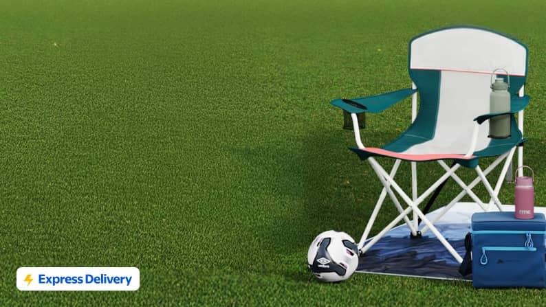 A blue and white camp chair, cooler, blanket, and soccer ball on a grassy field.
