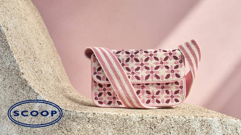 Beaded shoulder bag with pink and cream floral pattern and wide striped strap resting on a stone ledge against a pink wall.