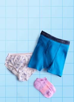 Flat-lay of kids' basics showing blue mesh athletic underwear alongside gray and pink patterned ankle socks on a light blue grid.