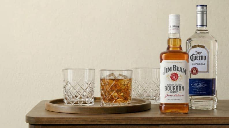 A tray of glasses, one with bourbon on ice, next to a bottle of Jim Beam bourbon whiskey and a bottle of Jose Cuervo Especial tequila.