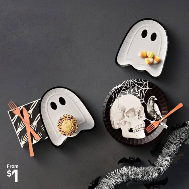 Halloween-themed paper plates, orange plastic flatware, a skeleton print napkin, silver tinsel and a bat-shaped cookie are shown. From one dollar.