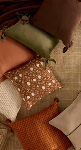 A mix of pillows in warm earthen colors and patterns is displayed on a jute rug.