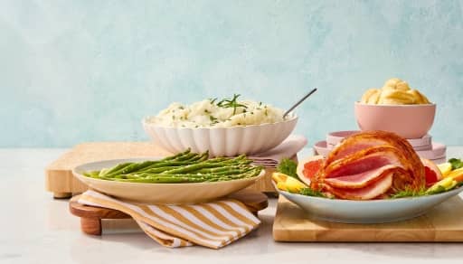 An Easter food spread is shown complete with ham, mashed potatoes, green beans and dinner rolls.
