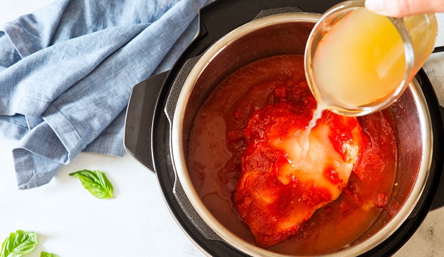 Pouring chicken broth into Instant Pot with tomato sauce and chickeen