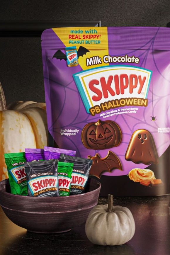 Skippy PB Halloween milk chocolate peanut butter candies in a purple bowl in front of a large Skippy PB Halloween bag with pumpkins.