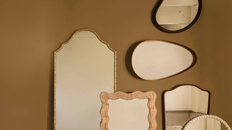 Wall mirrors in various shapes, including arched, scalloped and pebble designs, are displayed on an olive green wall.