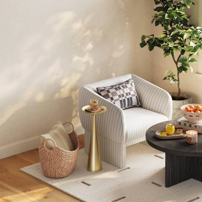 Image of striped accent chair with pillow, house plant, decorative pillow basket & a gold side table with drink.
