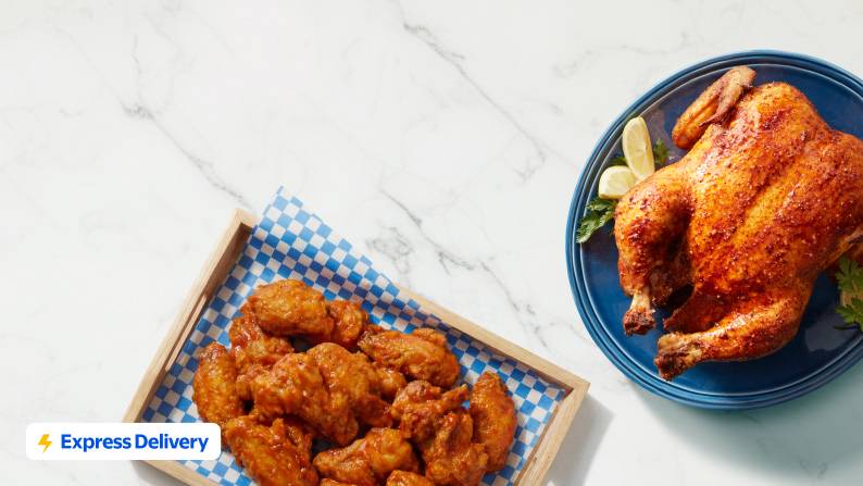 A rotisserie chicken on a blue plate and some chicken wings in a basket.