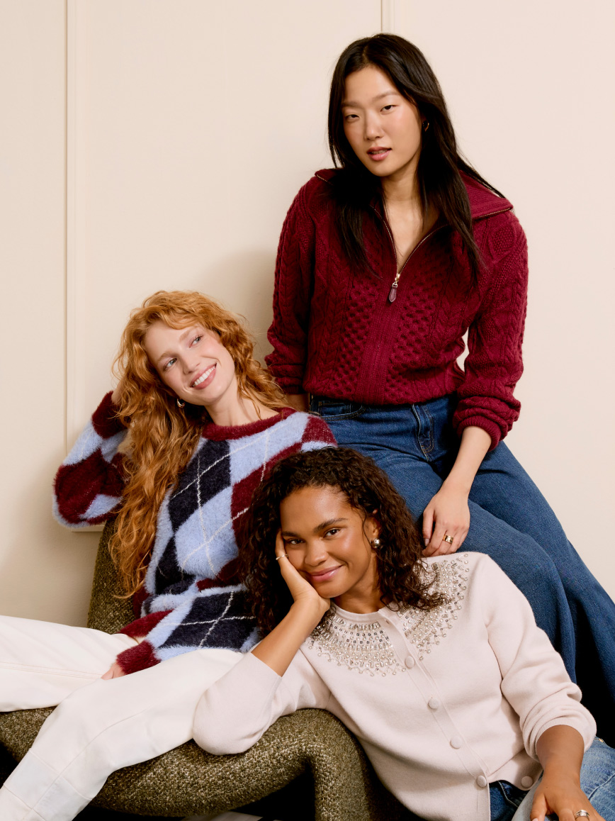 Three adults indoors wearing cozy knit sweaters, one in argyle, one in a zip neck pullover and one in a light embellished sweater.
