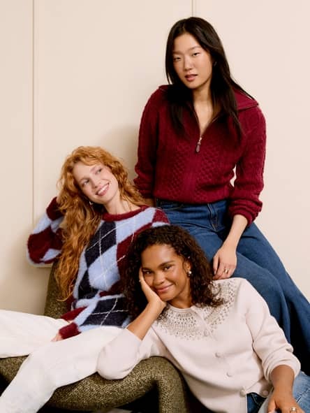 Three adults indoors wearing cozy knit sweaters, one in argyle, one in a zip neck pullover and one in a light embellished sweater.