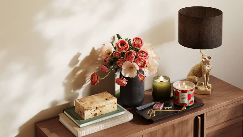A wooden console with pink flowers in a black vase, candles and a gold cheetah lamp. Reads: Summer decor spotlight. From five ninety-seven.