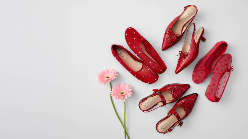 Two pink flowers are next to four pairs of red women’s shoes.