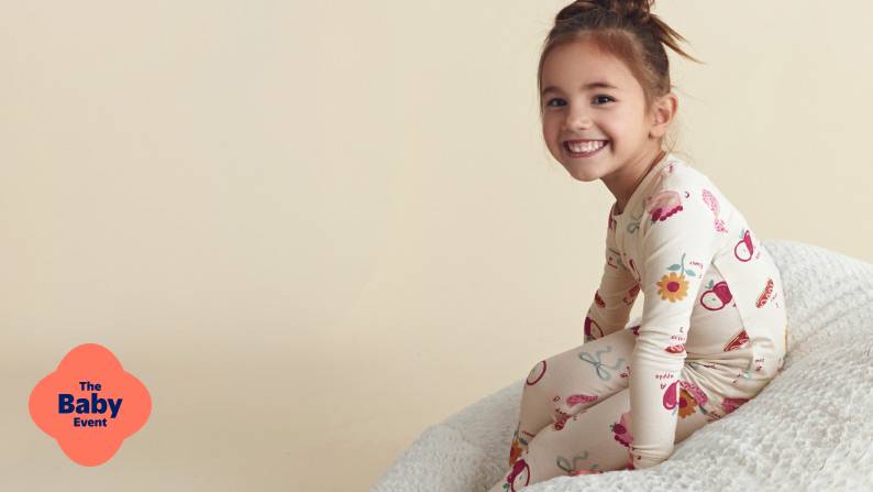 The Baby Event badge. A smiling child sits on a white surface wearing light pajamas with colorful illustrations.